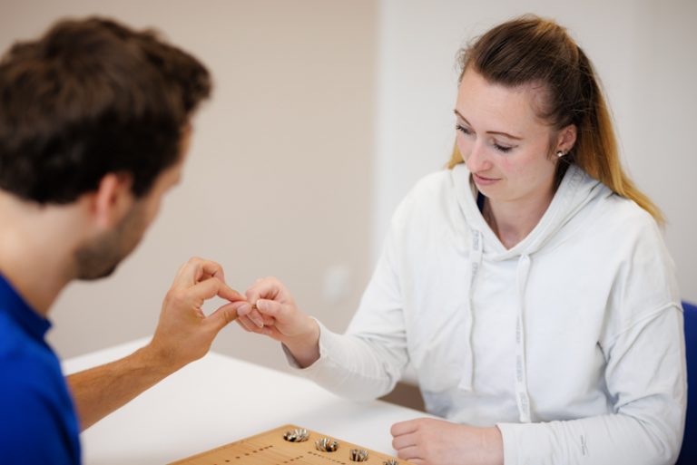 Der Fotograf dokumentiert eine therapeutische Sitzung, sei es in der Logopädie oder Physiotherapie. In der Logopädie arbeitet der Therapeut mit einem Patienten an Sprachübungen, während in der Physiotherapie manuelle Therapien durchgeführt werden. Der Fokus liegt auf der professionellen Behandlung und der ruhigen, vertrauensvollen Praxisatmosphäre.
