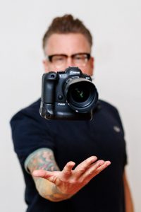 Fotograf Martin Valk aus Duisburg hält eine Canon Kamera in die Kamera – Business- und Imagefotograf im Ruhrgebiet